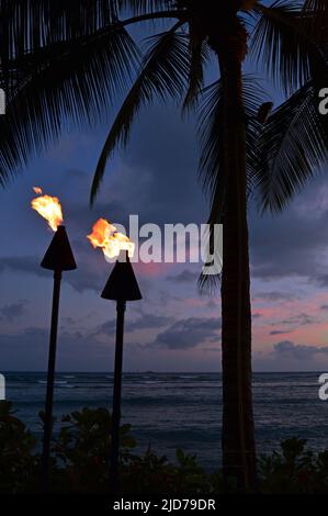 Due torce, parte di una tradizione culturale Hawaiiana, illuminano un cielo notturno tropicale lungo Waikiki Beach a Oahu nelle Hawaii Foto Stock