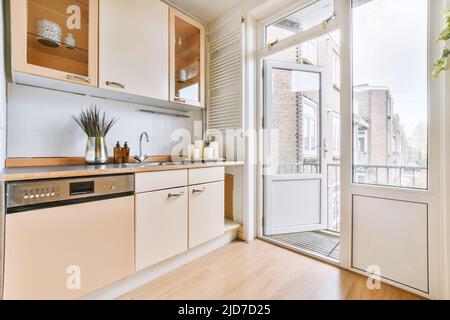 Interno di una cucina luminosa con mobili beige e porte balcone in un appartamento moderno Foto Stock