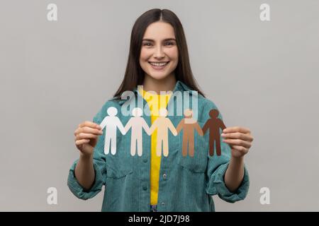 Ritratto di sorridente donna felice che tiene in mano catena di multiculturale carta persone, multinazionale razza concetto di unità, indossando casual stile giacca. Studio interno girato isolato su sfondo grigio. Foto Stock