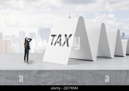 Fiscalità e strati fiscali concetto di consultazione con una donna d'affari pensiva di fronte alla grande cassetta di cassa con parola d'imposta su superficie concreta e città backgroun Foto Stock