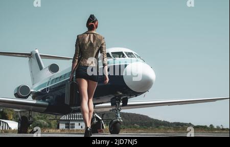 Stewardess in blu uniforme - vista posteriore. Piuttosto assistente di volo femminile in aeroporto. Affascinante stewardess vestita in uniforme blu. Viaggi e jet Foto Stock