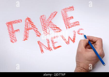 Notizie FALSE di scrittura. Iscrizione LE NOTIZIE FALSE sono rosse, disegnate con una matita blu su sfondo bianco. Scrivere a mano scrivere notizie FALSE. Propaganda nei media. Sostituzione dei concetti. Scrittura Handdraw. Foto Stock