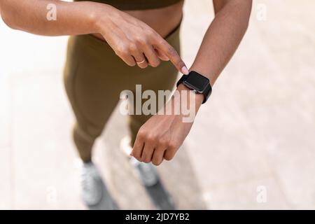 Giovane donna nera che usa il tracker di idoneità con mockup, controllando la frequenza cardiaca e le calorie bruciate mentre jogging sulla strada Foto Stock