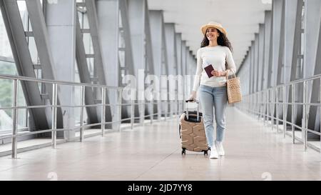 Viaggio di vacanza. Donna sorridente che indossa il cappello di paglia Passeggiate con i bagagli in aeroporto Foto Stock