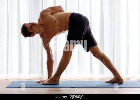 Giovane uomo che fa yoga triangolo posa al mattino Foto Stock