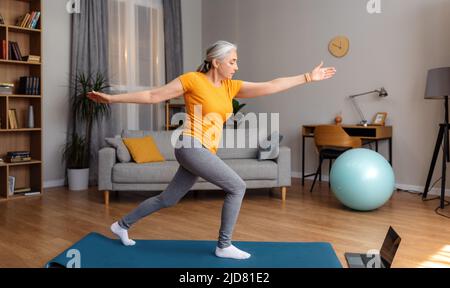 Corsi di yoga online. Donna anziana attiva che si esercita di fronte al laptop, avendo online lezioni di yoga a casa Foto Stock