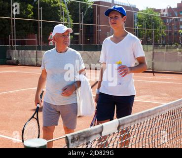 nonno e nipote parlano sul campo giocando a tennis Foto Stock