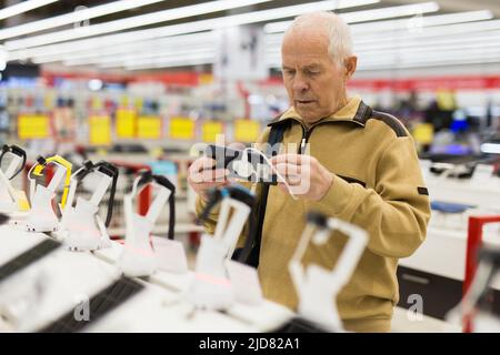 uomo anziano in grigio pensionato esaminano il contatore con gadget elettronici e tablet in showroom del negozio di merci digitali Foto Stock