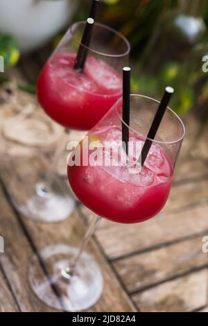 cocktail rosso con ghiaccio in vetro con gambo su superficie di legno Foto Stock