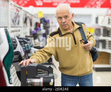 Uomo anziano che sceglie la felpa con cappuccio verticale nello showroom del negozio di elettrodomestici Foto Stock