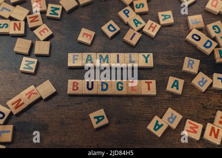 Importanza del bilancio familiare. Moderne lotte finanziarie familiari. Piccolo quadrato di legno colorato puzzle lettera su un tavolo marrone. Foto di alta qualità Foto Stock