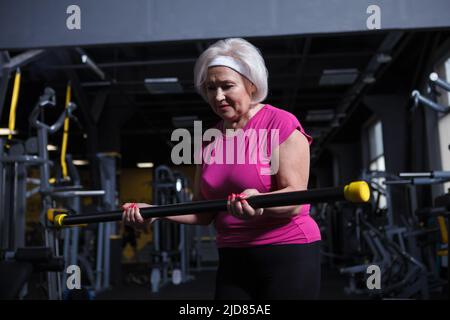 Donna anziana che osserva messa a fuoco, facendo i ricci del bicep Foto Stock