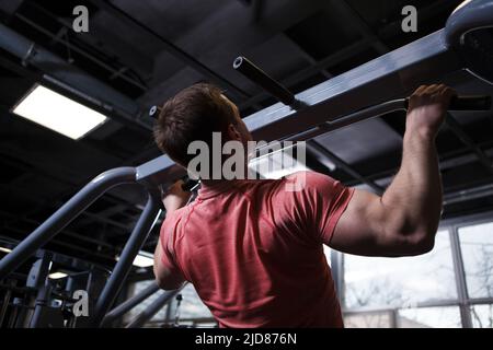Vista posteriore basso angolo scatto di un uomo muscolare facendo pull-up in palestra Foto Stock