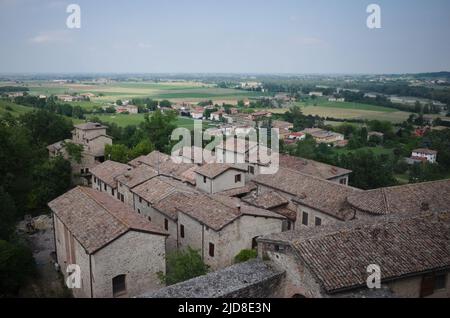 Torrechiara, Parma, Italia - Giugno, 2022: Vista dall'alto dei tetti in tegole di vecchie case in paese e valle con raccolti campi agricoli Foto Stock