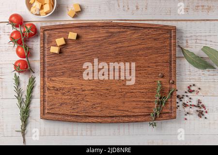 tagliere quadrate in legno con bordatura. pomodori ciliegini, fette di formaggio e spezie su sfondo bianco. mockup con spazio di copia per testo, vista dall'alto Foto Stock