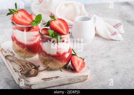 Cheesecake alla fragola. Cheesecake o trifle con fragola in vetro su sfondo vecchio tavolo grigio cemento. Cheesecake senza cottura. Dess Foto Stock