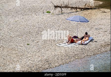 Monaco di Baviera, Germania. 19th giugno 2022. Una coppia si trova sotto il loro ombrellone su una riva di ghiaia vicino al fiume Isar. Credit: Peter Kneffel/dpa/Alamy Live News Foto Stock