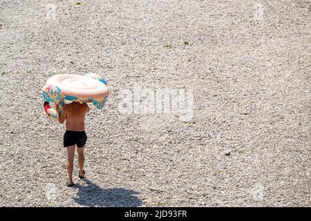 Monaco di Baviera, Germania. 19th giugno 2022. Un uomo porta un flamingo gonfiabile attraverso la ghiaia Isar all'acqua. Credit: Peter Kneffel/dpa/Alamy Live News Foto Stock