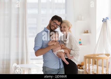 I giovani genitori che tengono le braccia sorridono il bambino guardano la macchina fotografica Foto Stock