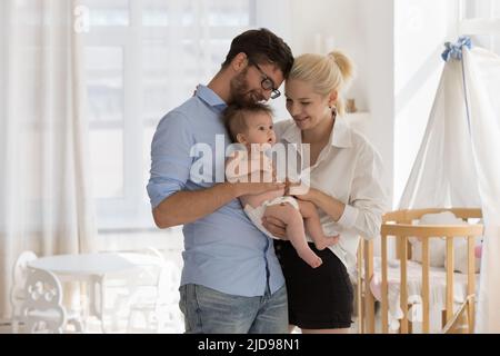 Giovani genitori amorevoli in piedi nella stanza dei bambini accogliente che tiene il bambino adorabile Foto Stock