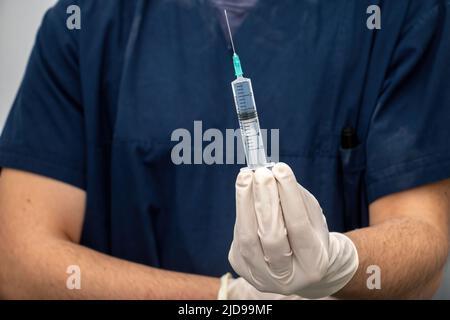 Il medico in uniforme medica tiene in mano con il guanto usa e getta, il farmaco liquido in siringa con l'ago e introdurlo. Assistenza sanitaria, trattamento da profess Foto Stock