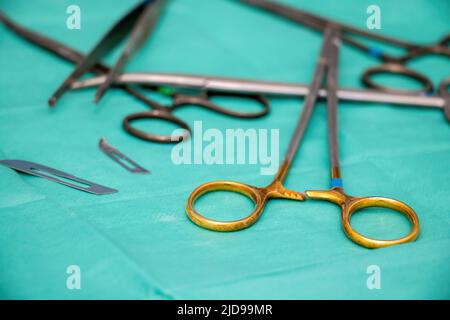 Strumento chirurgico sterilizzato su fondo tessuto verde. Medico chirurgo in acciaio inox utensile, lama, supporto ago o driver, forcipe di sfocatura e sciss Foto Stock