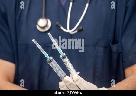 Medico in uniforme medica tiene, in mano con guanto monouso, siringa vuota. Offuscare il medico con lo stetoscopio intorno al collo. Concetto di assistenza sanitaria Foto Stock