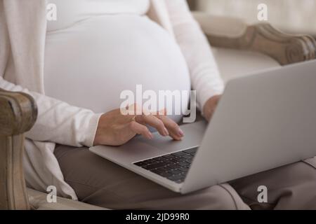 La donna incinta con un taglio corto si siede su una poltrona con un computer portatile Foto Stock