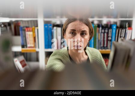Le donne di mezza età scelgono il libro dalla libreria in università, biblioteca universitaria per la ricerca di istruzione Foto Stock