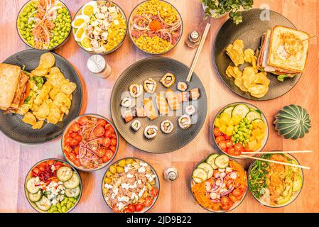 Set di ciotole piene di insalate, ciotole di poke in stile asiatico, insalata di pollo con mais, sushi assortito e due sandwich con patatine fritte Foto Stock