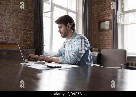 Un uomo d'affari che utilizza un computer portatile si siede alla scrivania con carte e calcolatrice Foto Stock