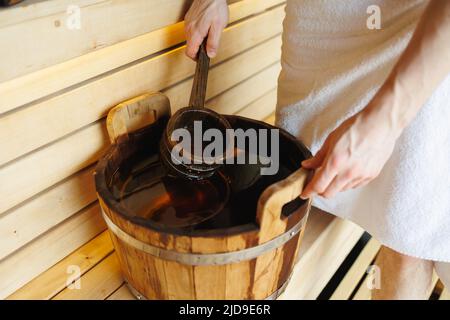 Primo piano di un uomo in una sauna raccogliere acqua con una mestola da un secchio di legno Foto Stock
