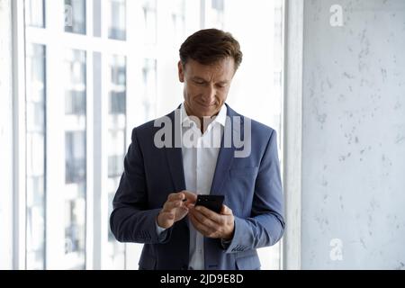 Uomo d'affari di mezza età in ufficio, controlla i messaggi sullo smartphone Foto Stock