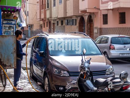 Un bambino che lava un'automobile usando l'acqua da un tubo flessibile. Bambini che lavorano per le strade di Essaouira, Marocco Foto Stock