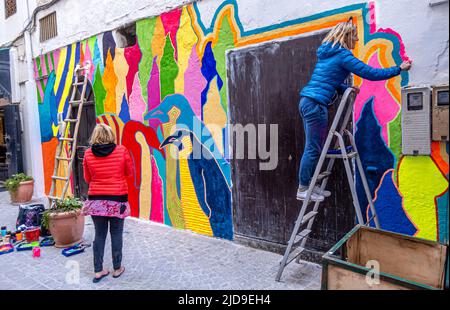 Artisti che dipinggono murale colorato sulla parete nel centro di Essaouira, Marocco Foto Stock