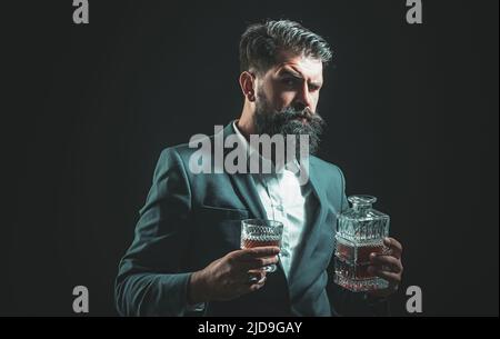 Uomo alla moda in maglietta bianca e branchi. Uomo che beve alcol dal vetro. Bevanda alcolica. Bere whiskey o brandy o cognac. Foto Stock