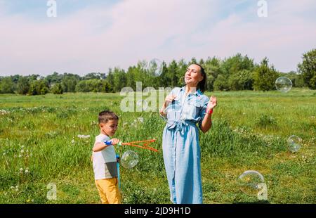 I preschoolers del figlio e della mamma trascorrono il tempo all'aperto in estate e soffiano le bolle grandi del sapone Foto Stock