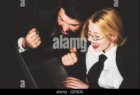 Coppia che è felice di vincere una scommessa nel gioco d'azzardo online sul suo notebook. Entusiasti uomini d'affari con notebook su sfondo nero Foto Stock