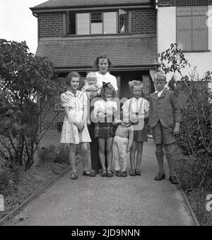 1940s, storica, una madre in piedi con i suoi figli per una foto, sul percorso di ingresso alla loro casa su Woodford Rd, vicino al villaggio di Bramhall, un prospero sobborgo di Stockport, Cheadle, Inghilterra, Regno Unito. Foto Stock