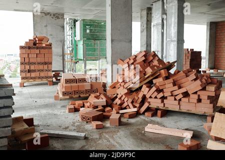 Interno di blocchi di appartamenti non finiti con colonne in calcestruzzo, pali di mattoni nuovi sul pavimento e altri materiali da costruzione Foto Stock