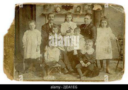 Originale, affascinante, angosciato, squallido ed elegante cabinet card vittoriano attraente grande famiglia vittoriana della classe media, 7 bambini, manifattura in un salone, ragazzi che indossano le tute Little Lord Fauntleroy. Dallo studio di Taylor Photographers, circa 1888, 1889. REGNO UNITO Foto Stock