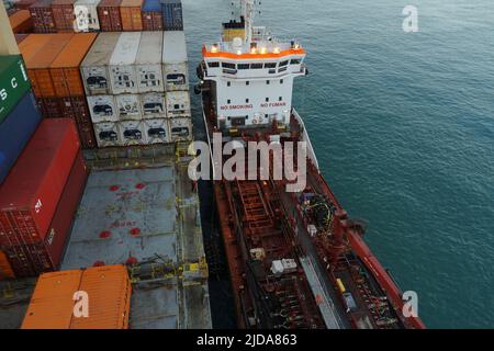 Vista aerea sulla chiatta del bunker con scafo rosso e sovrastruttura bianca accanto alla nave container caricata. Foto Stock