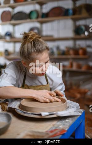 Un ceramista fa un piatto. Donna in grembiule lavora in un laboratorio di ceramica. Foto Stock