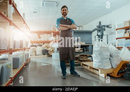 Il proprietario di affari sorridente sta in piedi sullo sfondo della macchina di tostatura del caffè Foto Stock