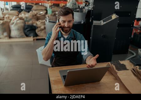 Il proprietario di affari che parla con il cliente mentre siede nella propria piccola fabbrica di caffè Foto Stock