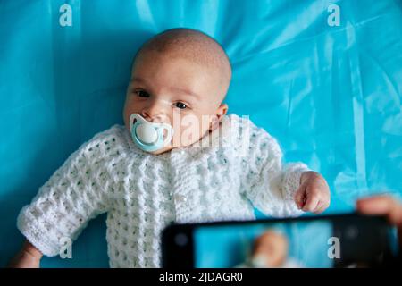 Il genitore fotografa il bambino con il succhietto in bocca utilizzando lo smartphone, scattato dall'alto Foto Stock