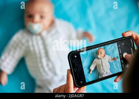 Il genitore fotografa il bambino sdraiato con lo smartphone, scattato dall'alto Foto Stock