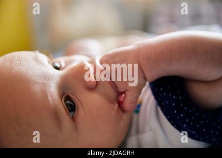 Primo piano di un bambino di tre mesi che si stendeva e succhiava le dita Foto Stock