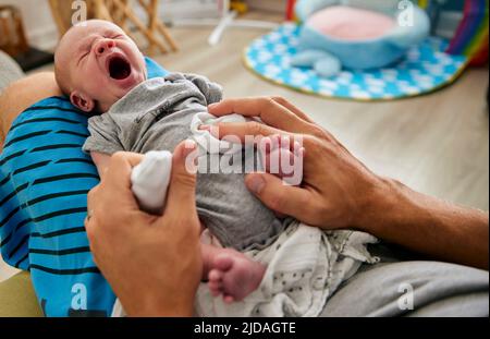 Le mani del padre che tengono il bambino di tre mesi yawning sul grembo, all'interno. Foto Stock