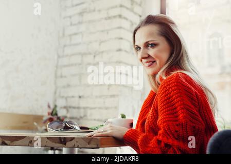 Donne piuttosto giovani che bevono caffè caldo in un caffè. Persona che tiene una tazza di cappuccino sopra la finestra mentre riposa in città. Ospite che ha un freno corto Foto Stock